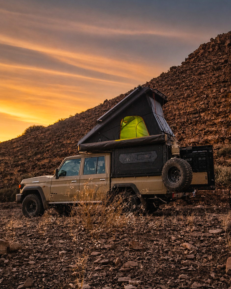 Camping-equipped 4x4 with rooftop tent beside rocky hills at sunset