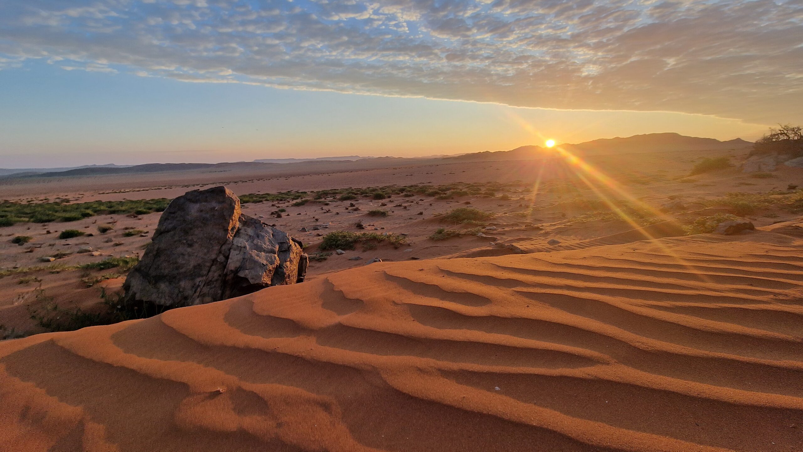 Low sunlight over rippled Namib dunes and rocky outcrops